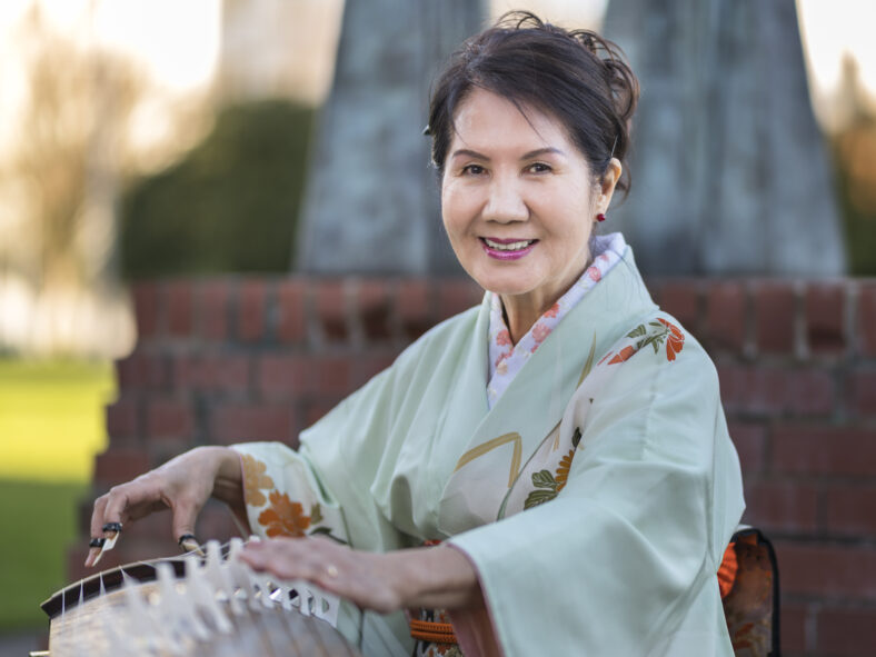 Masumi Timson dressed in a light green kimono posed with her koto outside