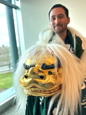 A man in a green and white jacket holding a golden lion head for the Shishimai traditional Japanese lion dance