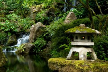 A stone lantern on a rock with moss covered top above the koi pond in the Portland Japanese Garden